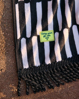 Black and white striped beach towel with a fringed edge and a yellow label that reads ’carry your life with love.’