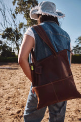Brown leather tote bag with sturdy handles and a small green tag on the strap.