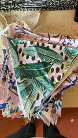 A colorful triangular fabric banner with tropical leaf and polka dot patterns in green, brown, and pink.