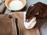 A hand gently buffs a tan leather jacket with a soft white cloth.