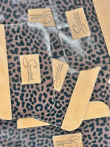 Leopard-print transparent phone case with tan leather trim and branded suede patch.