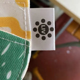 White fabric care label with a black circular logo featuring the letters ’ln’ surrounded by dots.