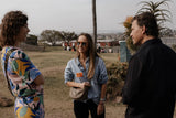 The woman in the center wears a light blue denim jacket over black pants, accessorized with sunglasses and a small beige textured crossbody bag.