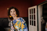 Woman wearing a colorful floral print top with yellow, blue, and green leaves on a light background