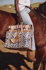 Zebra-print travel bag with tan leather straps and a palm tree charm.